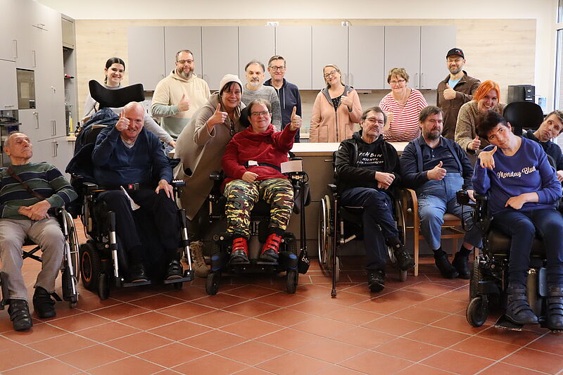 Zwei Reihen an Personen, die den Daumen hoch zeigen. In der Ersten sitzen Rollstuhlfahrer.